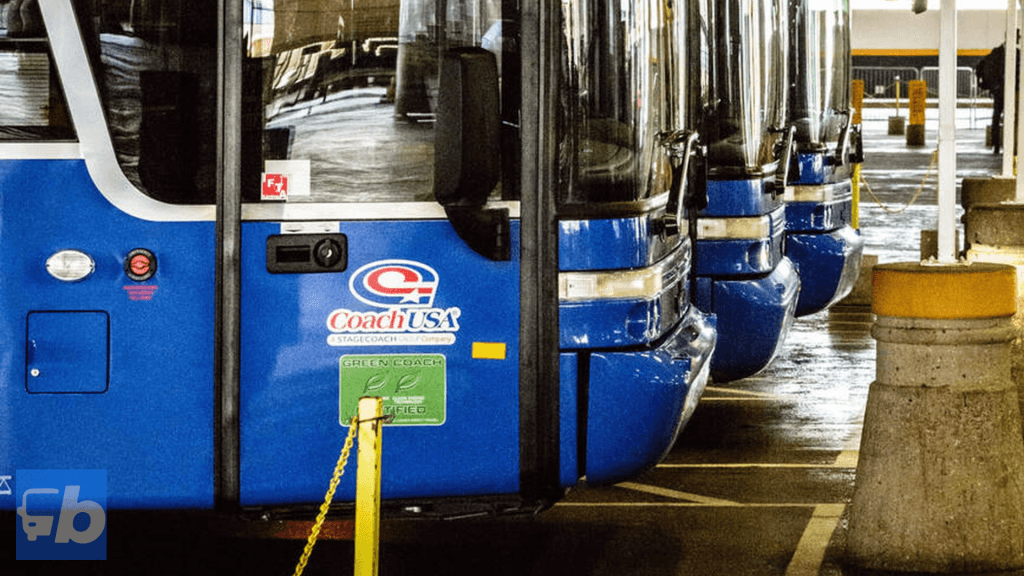 A close-up view of multiple Coach USA operated by Megabus buses parked in a row inside a bus terminal. The buses are lined up with their distinctive blue and white branding, showcasing the "Coach USA" logo and the "Green Coach Certified" badge. The indoor terminal setting emphasizes the well-organised and professional service provided by the company.