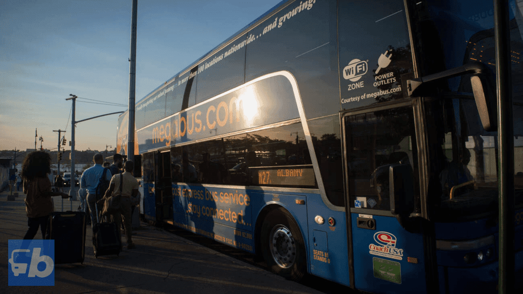 A Coach USA operated by Megabus. A group of passengers boarding a Megabus in the late afternoon or early evening as the sun sets. The sunlight reflects off the side of the double-decker bus, highlighting the "megabus.com" branding and the route display showing "M27 Albany." The bus is equipped with amenities such as Wi-Fi and power outlets, as indicated by the decals on the windows. The scene captures the relaxed, yet active moment of travelers embarking on their journey.